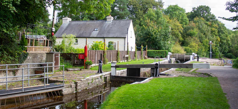 A view of the lock and lock cottage at Brynich south of Brecon. The lock is empty and the grass and trees are vibrant and green.