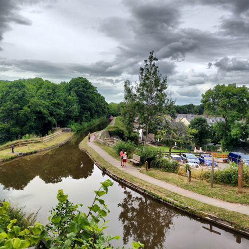 Looking down on the canal passing above Talybont village with dark brooding skies above. Two people are walking along the towpath.
